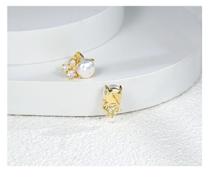 Detailed close-up of golden pearl earrings with zircon accents on a white display