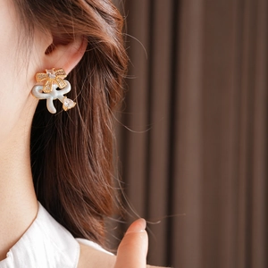 Close-up of golden bow stud earrings with white enamel and sparkling zircons on model
