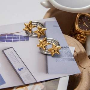 Elegant gold star and silver curved stainless steel stud earrings on a wooden display