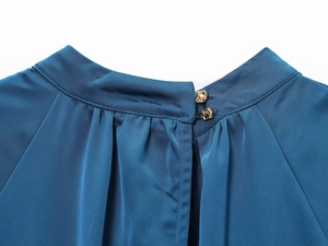 Detail of high neck teal satin dress with gold buttons and pleated neckline texture