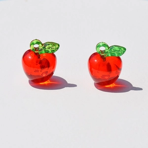 Detail view of two transparent red apple acrylic pendants with green leaves for DIY jewelry