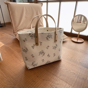 Close-up of floral canvas tote bag with brown leather handles and metal rivet details