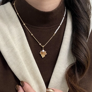 Close-up of 18K gold maple leaf pendant with asymmetrical pearl beaded necklace chain