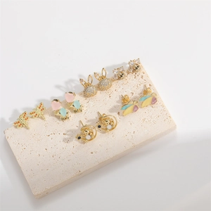 Detailed macro view of gold-plated animal stud earrings with enamel on travertine base