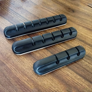 Three multi-slot black silicone cable organizers with adhesive backing on wood surface