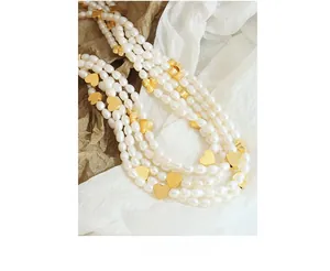 Detail of layered freshwater pearl necklace with gold heart charms on soft fabric background