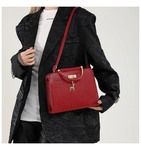 Detail of red crocodile texture handbag with golden deer pendant and metal handle bar
