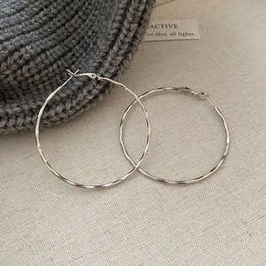 Detail of silver hoop earrings with wavy hammered texture on warm knit background