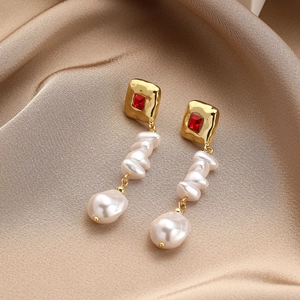 Detail of long baroque pearl earrings with red zircon insets on champagne silk fabric