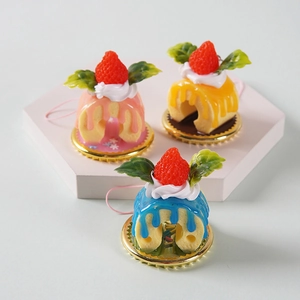 Tres colgantes de mini pasteles de fresa en rosa, azul y amarillo con bases doradas