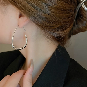 Side view of woman wearing large silver teardrop hoop earrings with high metallic gloss