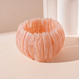 Détail d'un bracelet géométrique en résine marbrée rose sur un socle minimaliste