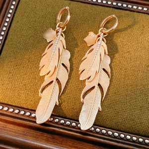 Detailed close-up of diamond-encrusted feather drop earrings in a green velvet box