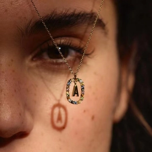 Detailed macro view of gold oval pendant with rainbow zircon stones and capital letter A