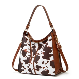 Detail of cow print shoulder bag showing brown leather straps and gold zipper hardware