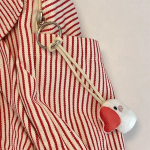 Macro detail of red striped canvas bag featuring a cute white plush heart keychain charm