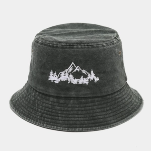 Dettaglio di un cappello pescatore slavato con ricamo bianco di montagne e foresta.