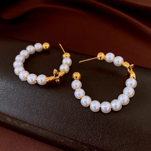 Detail of C-shaped gold-plated pearl earrings with a four-petal flower charm