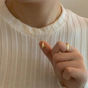 Detail shot of the V-shaped golden pendant and ring set worn on model with white knitwear