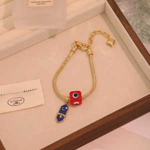 Detail of gold snake chain bracelet featuring evil eye, bee pendants on display tray