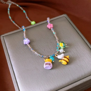 Close-up of beaded necklace with colorful flower, bee and honey pot pendants on box