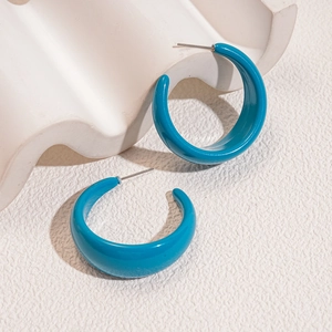 Detail view of blue C-shaped acrylic earrings on white textured background with silver pins