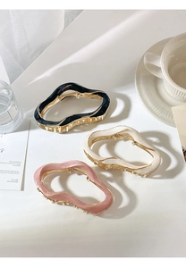 Three wavy metal hair claws in black, cream and pink displayed on a white table