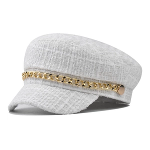 Macro shot of white tweed newsboy hat featuring textured weave and golden chain detail