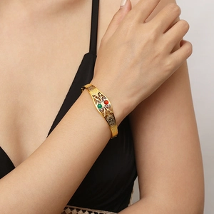 Close-up of gold geometric open bangle featuring red and green gemstones on model