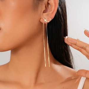 Close-up of golden bow earrings with long tassel chains worn by a model
