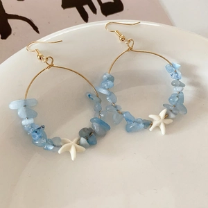 Macro shot of blue gemstone beaded hoop earrings with a white starfish charm on a plate