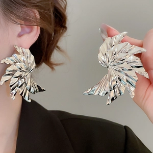Macro shot of large silver pleated swirl earrings featuring polished metallic texture