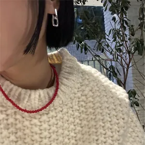 Dettaglio della collana minimalista di perline rosse con maglia bianca.