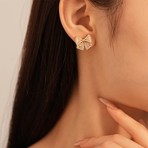 Close-up of a delicate golden bow earring with pearls and zircons on a female ear