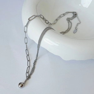 Detail of silver asymmetric chain necklace with sphere pendant on white ceramic bowl