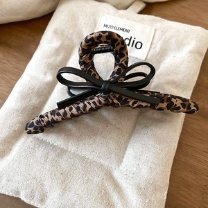 Detailed view of leopard print hair claw with black faux leather bow on canvas