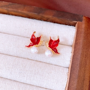 Gros plan détaillé des boucles d'oreilles papillon en émail rouge et perles blanches