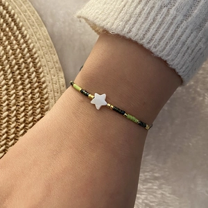 Close-up of beaded bracelet with green and black beads and white star charm on wrist