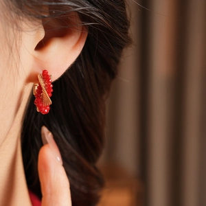 Macro detail of twisted gold hoop earrings with faceted red beads on a model