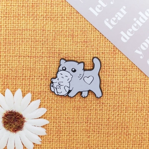 Close-up of cute grey mother cat carrying kitten enamel pin on orange woven fabric