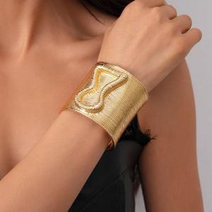 Detailed view of golden cuff bracelet with linear texture and embossed hourglass shape