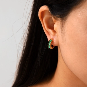 Detail of gold-plated stainless steel huggie hoop earrings set with green zircon stones