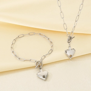 Detailed view of silver heart pendant necklace and bracelet set on soft silk fabric