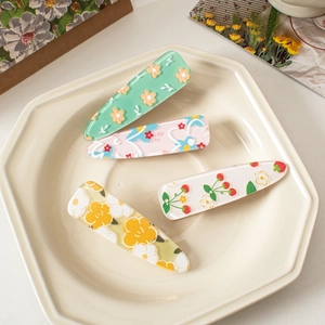 Detail view of colorful floral acrylic hair clips and duckbill pins in a ceramic tray