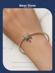 Detail of silver mesh bracelet featuring a turquoise heart and three feather charms