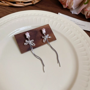 Détail de boucles d'oreilles à pompons argentés avec rose rose sur support bois