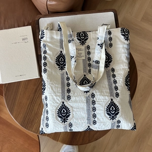 Close-up of ethnic embroidery pattern on beige cotton tote bag with brand label