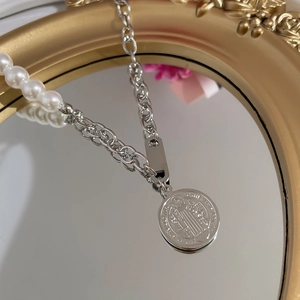 Close-up of pearl necklace with silver chain link and round pendant detail