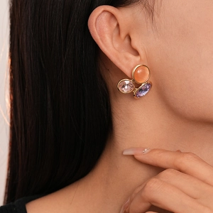 Détail de boucles d'oreilles géométriques avec œil de chat orange et cristaux roses