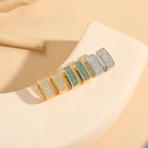 Detailed view of U-shaped gold and silver earrings with square zircon on beige display
